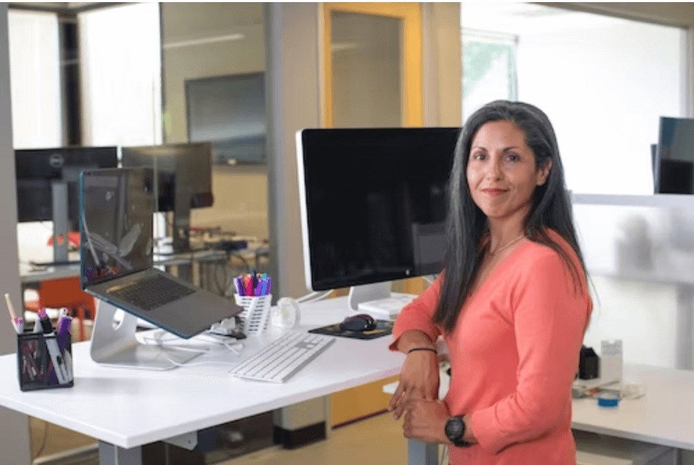 woman in orange shirt standing by computer