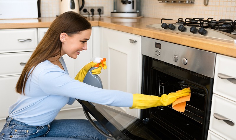 happy woman cleaning kitchen furniture using spray JMHGH3N